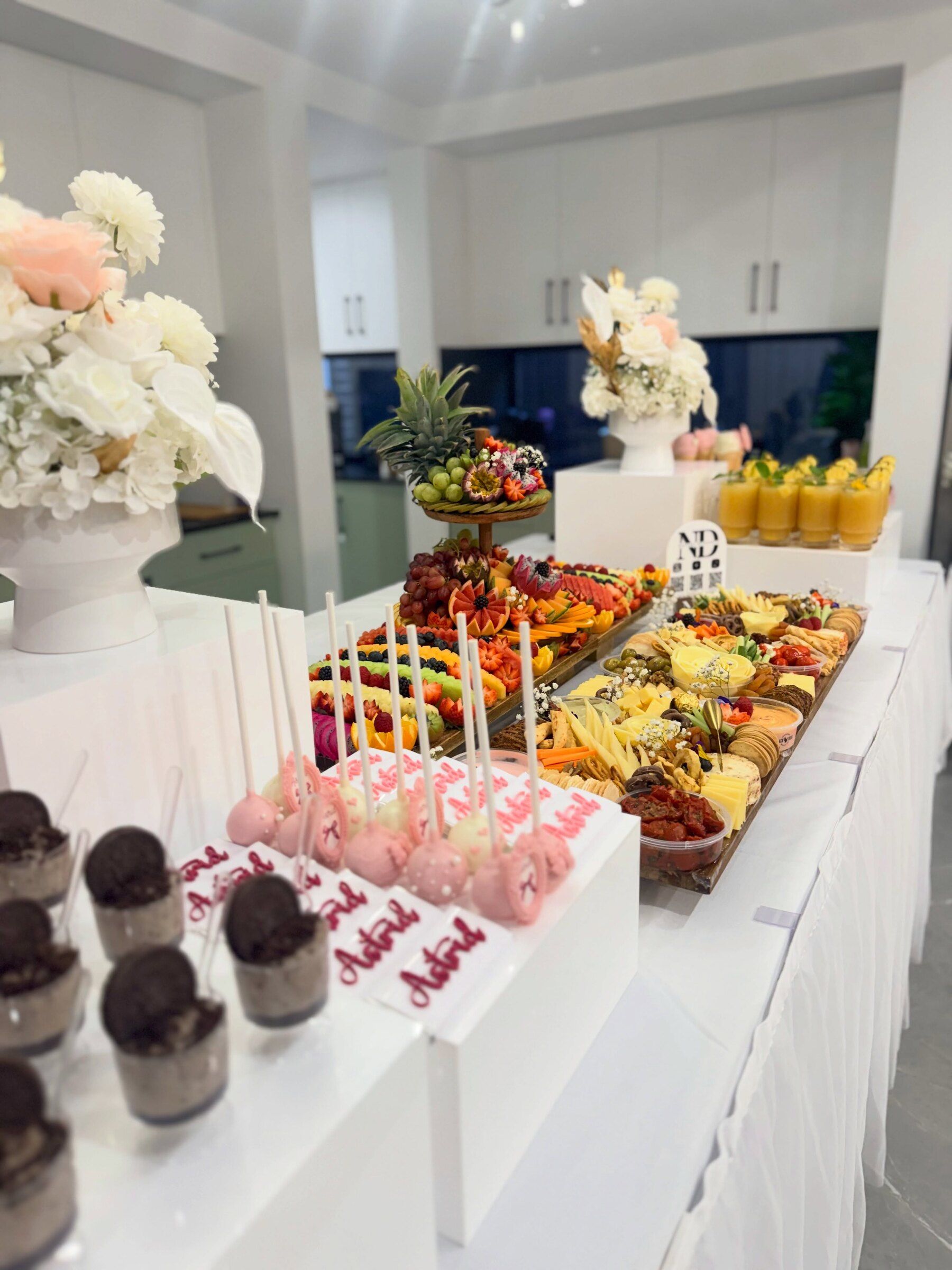 A soft pink baby shower table with grazing boards, cake pops and dessert cups