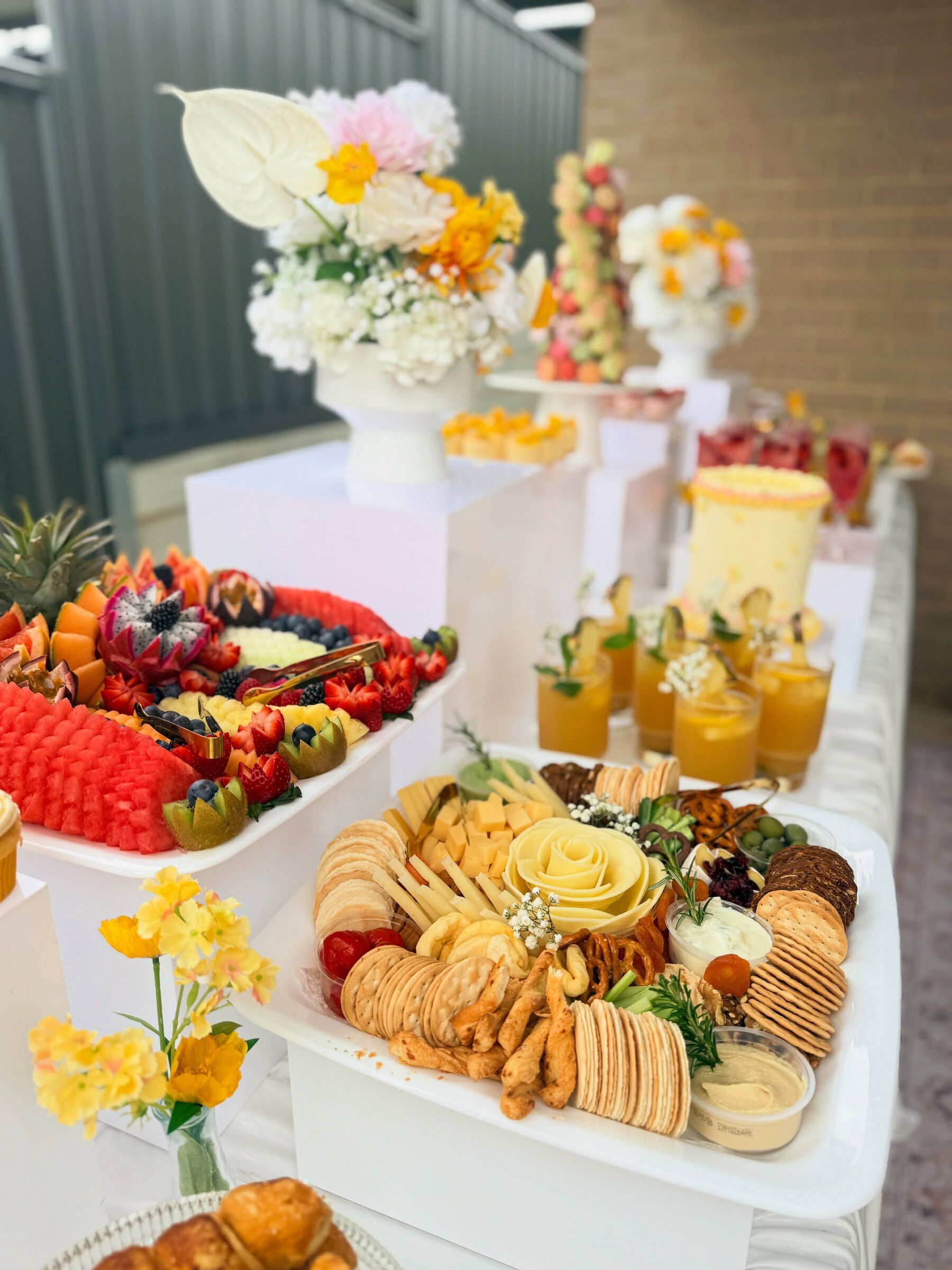 A pink and yellow baby shower table with fruit, grazing, mocktails and florals