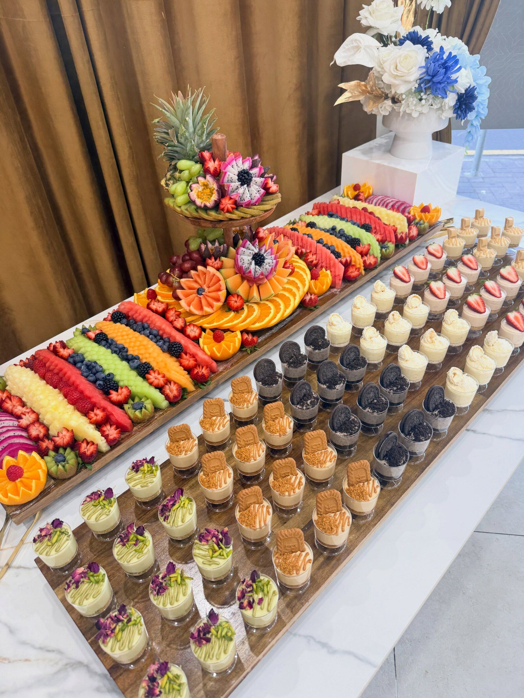 A fruit board with a carved tier next to rows of cheesecake dessert cups