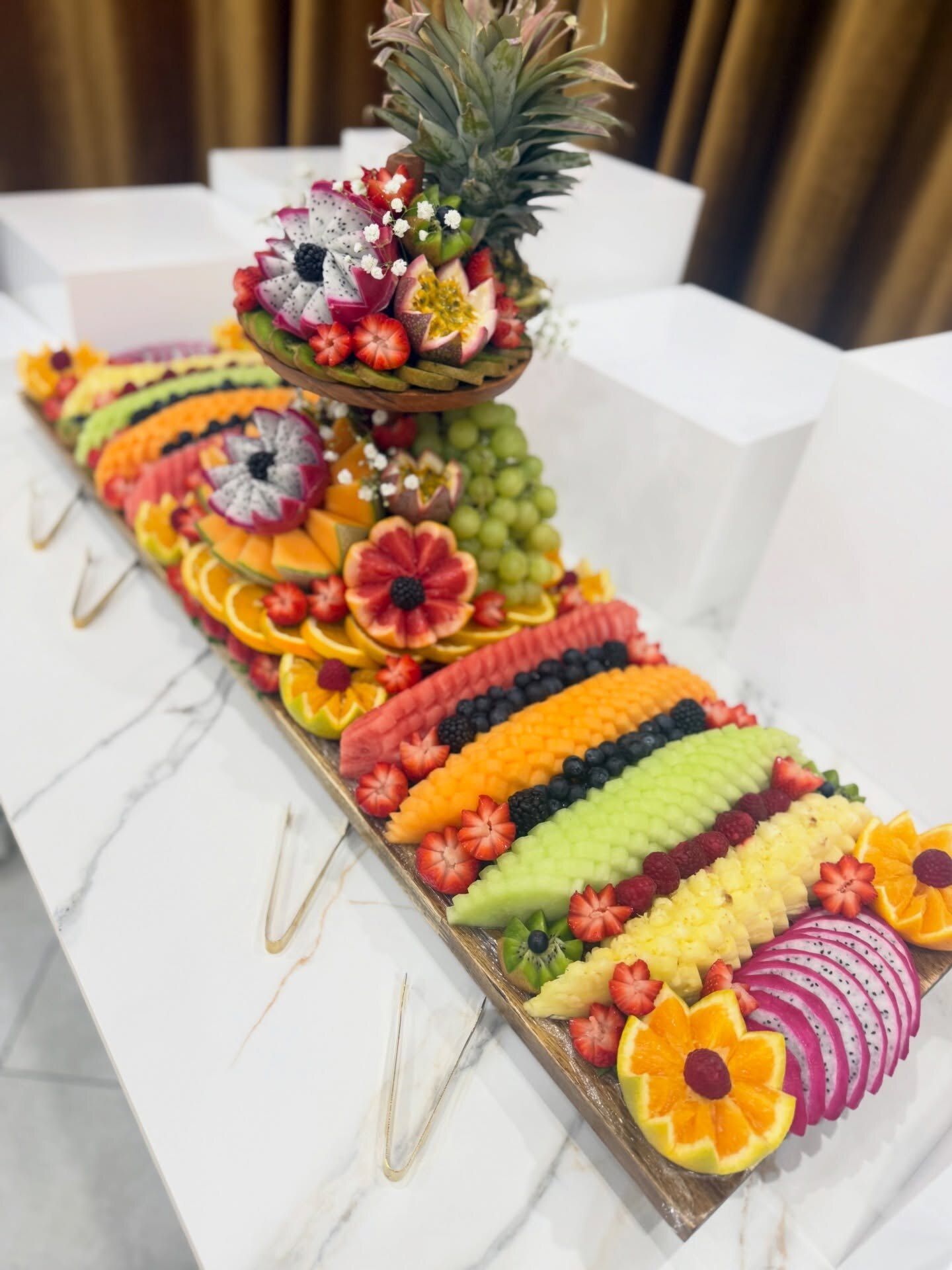 A long fruit board with a carved tier on white marble, framed by white plinths