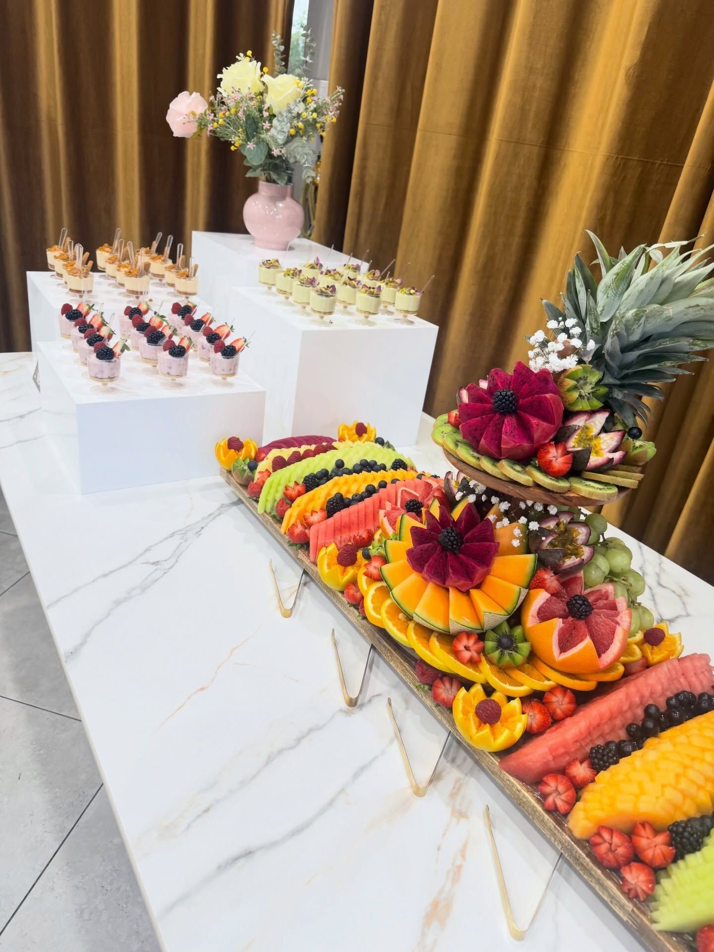 A fruit board with tier and dessert cups on white plinths for a gender reveal