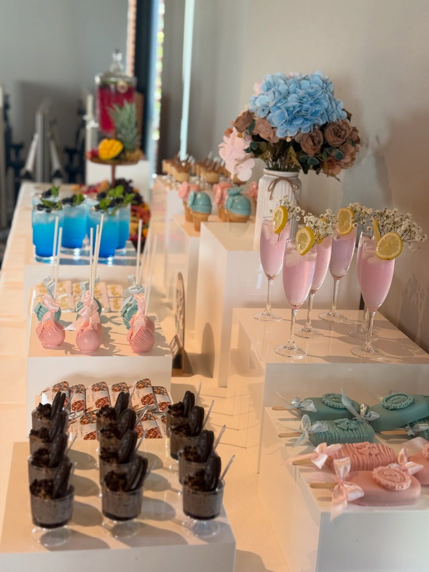 A pink and blue gender reveal table with mocktails and desserts