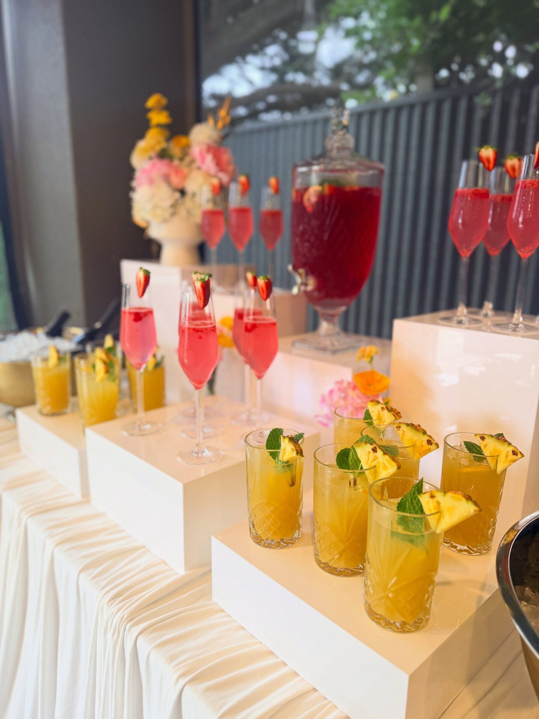 Pink lemonade and pineapple mocktails on white plinths with a glass dispenser and florals